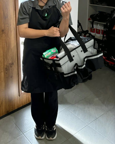 道具のバッグを持ち、玄関でごあいさつするエプロン姿のスタッフ